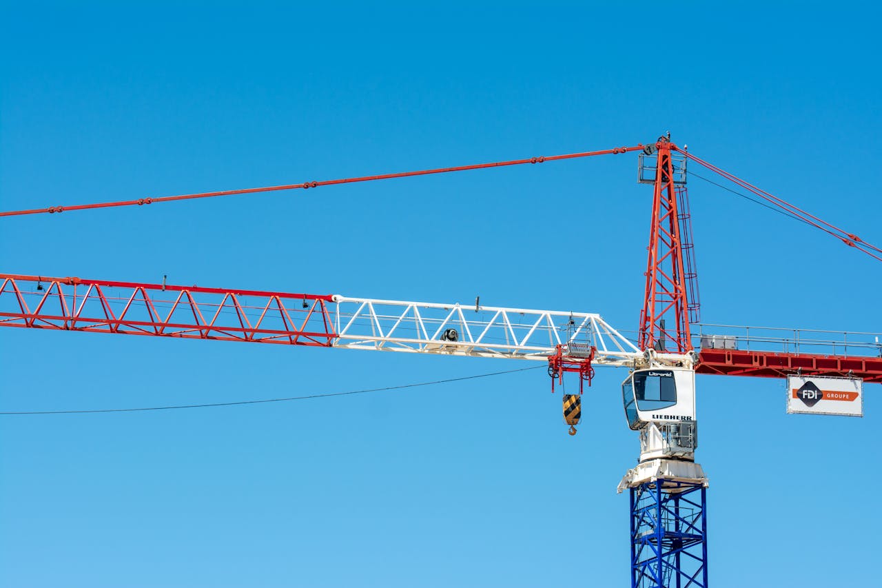 A striking view of a red and white tower crane set against a clear blue sky, symbolizing modern construction.