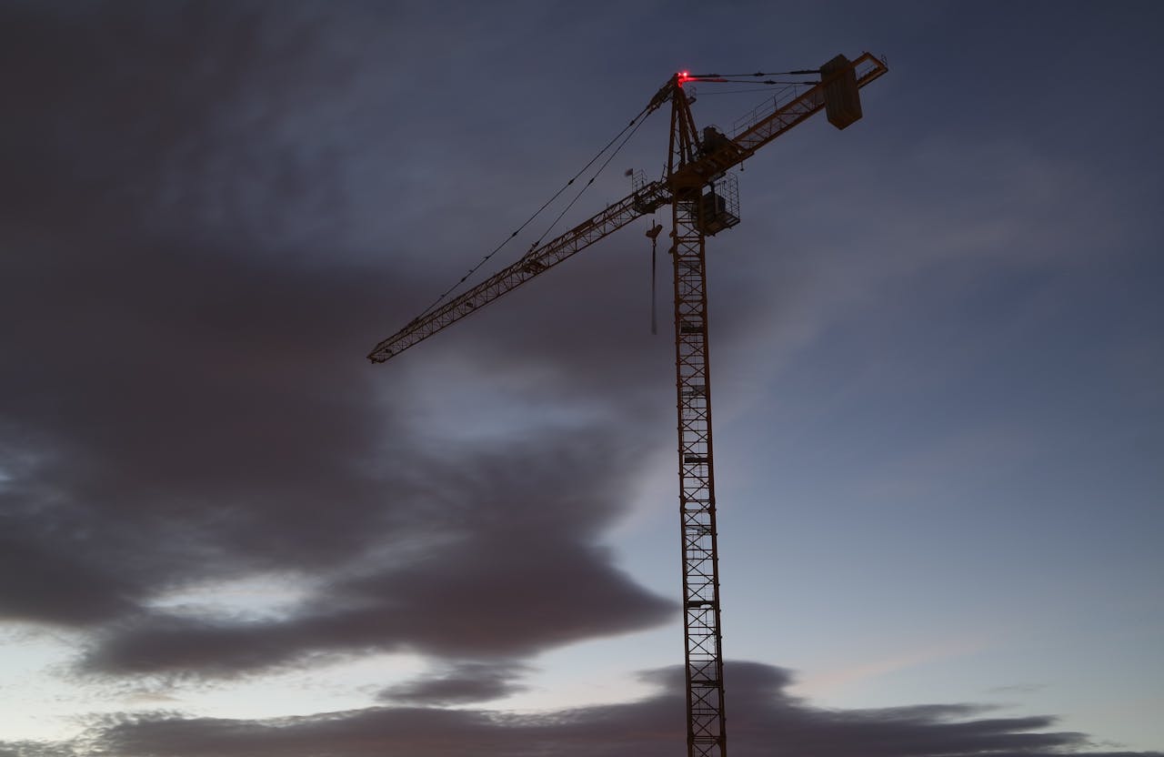 Silhouette of a tower crane with vibrant sunset clouds, depicting urban construction and development.